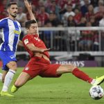 Obrazek przedstawia Roberta Lewandowskiego z Bayernu Monachium z piłką oraz piłkarza Herthy Berlin w tle podczas meczu